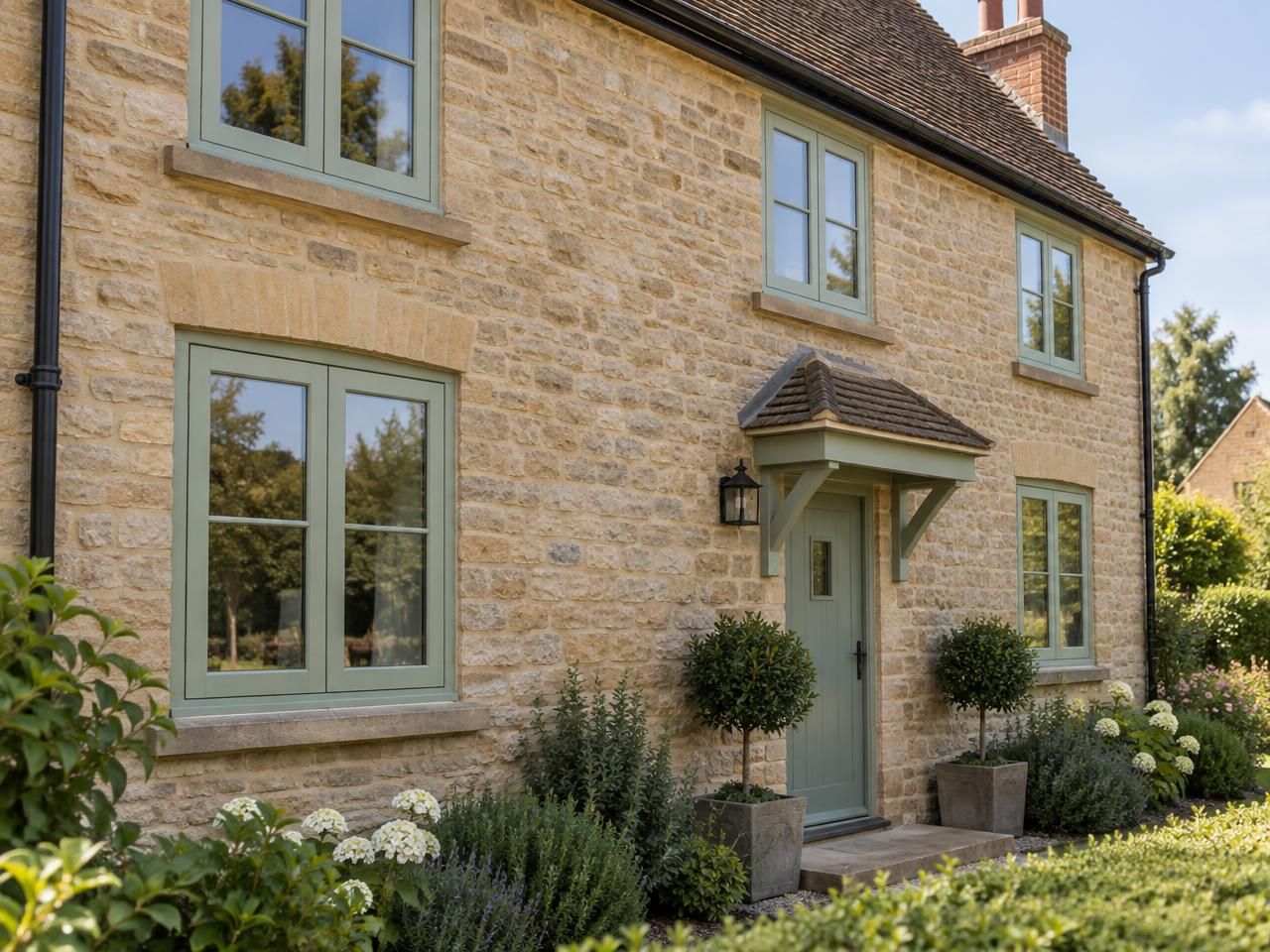 Chartwell green uPVC casement window on a honey-coloured Cotswold stone cottage with climbing roses at golden hour